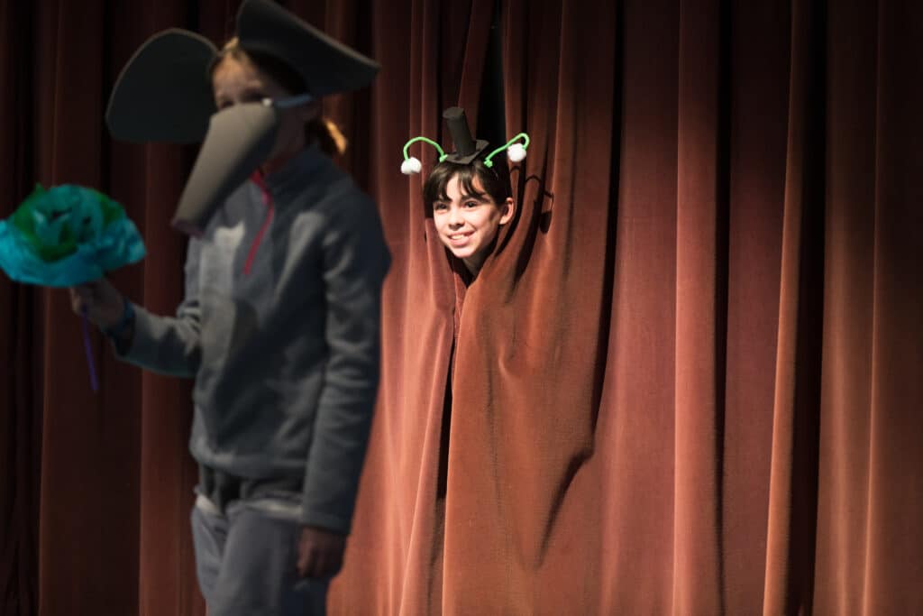 student peeks through the stage curtain